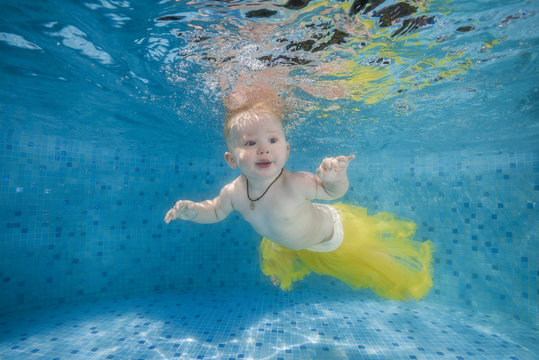 A little girl in a yellow skirt swims underwater in the pool