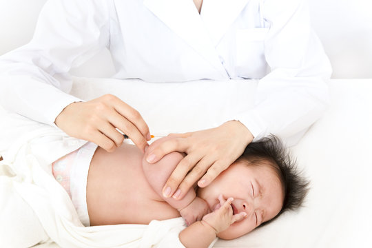 医師(看護師)により腕に注射を打たれ泣いている新生児の赤ちゃん。予防接種、インフルエンザ、病気、治療イメージ