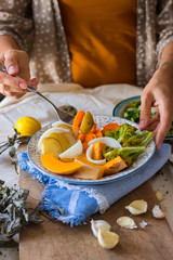 Woman hands holds steamed cooked assorted vegetables. Carrots, pumpkin, roasted potato, onion rings, broccoli. Seasonal vegan lunch, vegetarian autumn dinner, healthy food. With herbs, spices.
