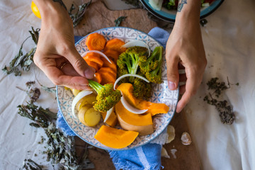 Woman hands holds steamed cooked assorted vegetables. Carrots, pumpkin, roasted potato, onion rings, broccoli. Seasonal vegan lunch, vegetarian autumn dinner, healthy food. With herbs, spices.