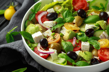 Healthy low calories salad with lettuce, heirloom tomatoes, avocado, feta cheese, red onion, cucumber, sweet peas, olives, thyme, mint and basil.