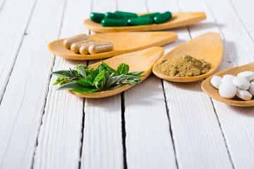 herbal leaves, ground herb powder and medicament pills on bamboo spoons, white wooden table