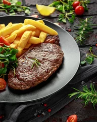Zelfklevend Fotobehang Grilled sirloin steak with potato fries and vegetables, tomato salad in a black plate. rustic table © grinchh
