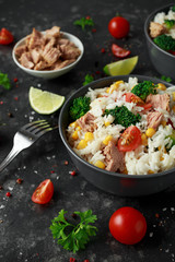 Fresh Tuna rice salad with sweet corn, cherry tomatoes, broccoli, parsley and lime in black bowl
