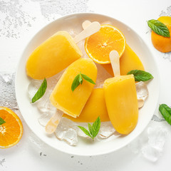 Popsicles, ice lollies on stick with sweet orange juice in white plate with ice
