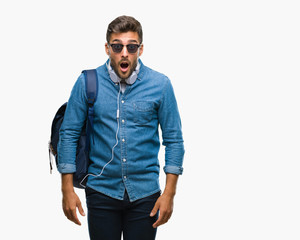 Young handsome tourist man wearing headphones and backpack over isolated background afraid and shocked with surprise expression, fear and excited face.