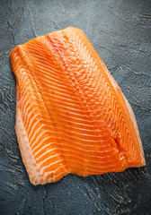 Raw salmon fillet on dark stone background