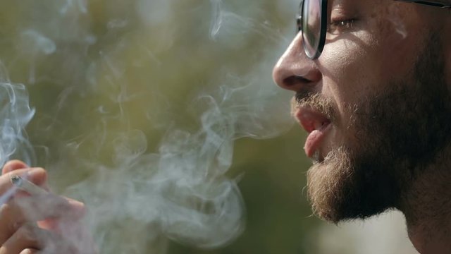 Man smoking a rolled up cigarette. Close up shot of man's hand and mouth. Man smoking a joint with cannabis