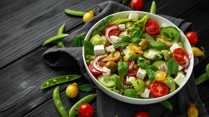 Healthy low calories salad with lettuce, heirloom tomatoes, avocado, feta cheese, red onion, cucumber, sweet peas, olives, thyme, mint and basil.