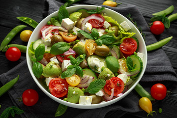 Healthy low calories salad with lettuce, heirloom tomatoes, avocado, feta cheese, red onion, cucumber, sweet peas, olives, thyme, mint and basil.