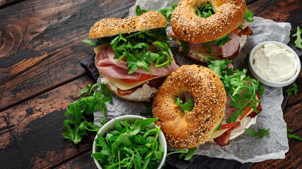 Fresh Bagels Sandwiches with cream cheese, bacon, tomato and green wild rocket on rustic wooden...