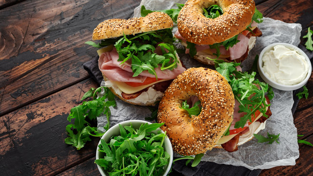 Fresh Bagels Sandwiches with cream cheese, bacon, tomato and green wild rocket on rustic wooden table
