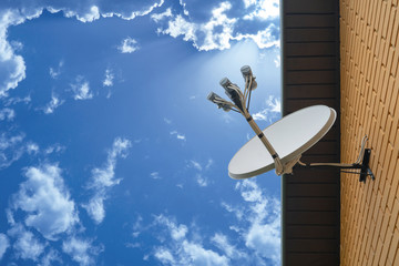 Satellite dish antenna mounted on the wall of a private house on blue sky background