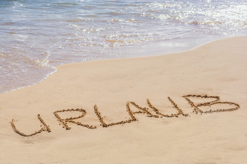 Fototapeta premium Sandstrand mit Meer im Hintergrund und dem Wort Urlaub in deutscher Sprache