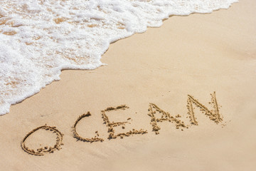 Sandstrand mit Brandung und dem in Sand geschriebenen Wort Ocean
