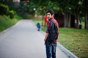 Young indian student man at red checkered shirt and jeans with backpack posed at street.