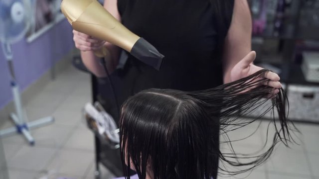 Slow-motion shooting close-up steadikam hairdresser stylist levels the client's dry hair with a curling iron, combs a lock of hair after applying keratin.