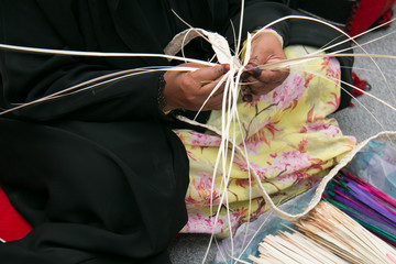 Hands of emirati woman who is weaving traditional basket from dry palm leaves