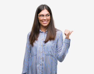 Young beautiful hispanic business woman smiling with happy face looking and pointing to the side with thumb up.