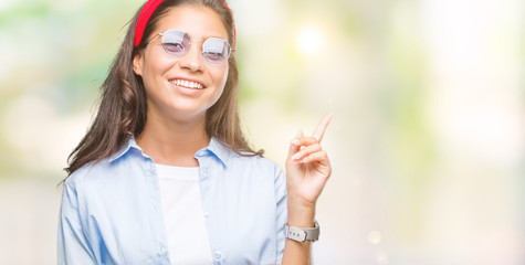 Young beautiful arab woman wearing sunglasses over isolated background with a big smile on face, pointing with hand and finger to the side looking at the camera.