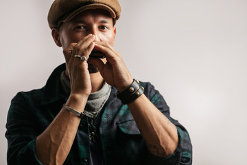 Caucasian maustached male traveler, wearing trendy cap playing a harmonica and looking at camera,...