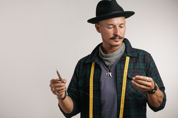 Successful leather goods craftsman with whiskers in stylish hat and measure tape around neck,...
