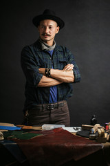 Portrait of handsome Leather goods craftsman in stylish hat doing handbags and leather accessories...