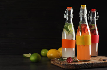 Bottles with natural lemonade on table against dark background
