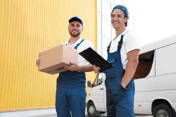 Male movers with box and clipboard near van outdoors