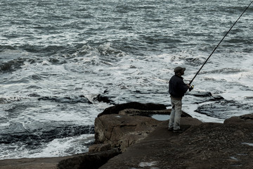 Hombre no reconocible pescando en las rocas con el mar de fondo