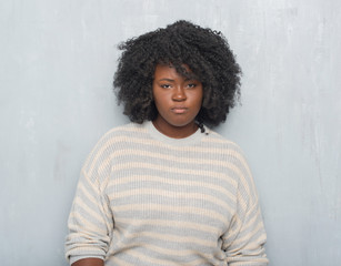 Young african american plus size woman over grey grunge wall wearing a sweater skeptic and nervous,...
