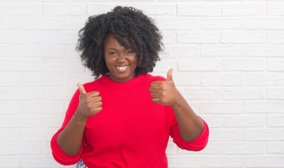 Young african american plus size woman over white brick wall success sign doing positive gesture...