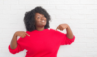Young african american plus size woman over white brick wall looking confident with smile on face,...