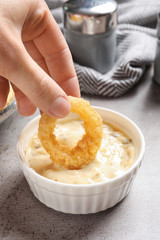 Woman dipping homemade crunchy fried onion ring in sauce on table, closeup