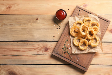 Homemade crunchy fried onion rings and tomato sauce on wooden background, top view. Space for text
