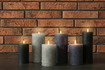 Burning candles on table against brick wall