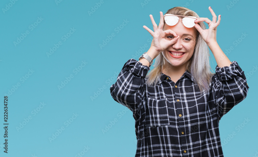 Wall mural young blonde woman wearing sunglasses over isolated background doing ok gesture with hand smiling, e