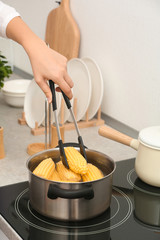 Woman preparing corn in stewpot on stove, closeup