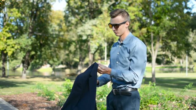 Young businessman outside in the park using mobile phone smartphone, putting suit jacket blazer and walking away