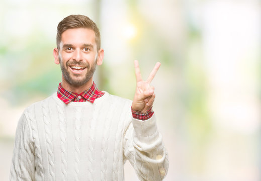 Young handsome man wearing winter sweater over isolated background smiling with happy face winking at the camera doing victory sign. Number two.