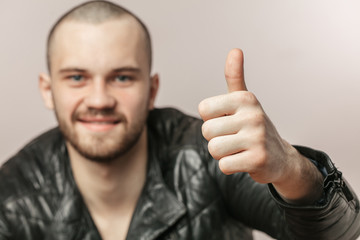 brutal strong bearded man in stylish leather jacket showing thumbs up. success, happinesss, agreement concepts. close up portrait. focus on the thumb up. blurred man's face