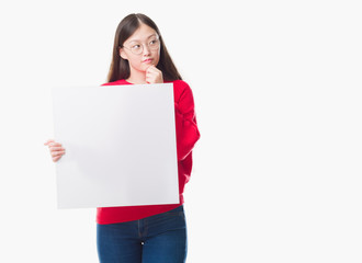 Fototapeta premium Young Chinese woman over isolated background holding blank banner serious face thinking about question, very confused idea