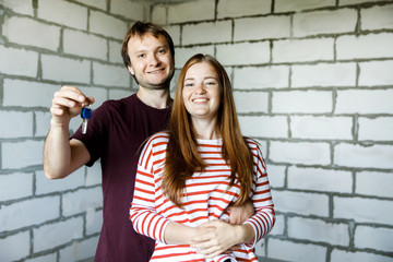Obraz na płótnie Canvas Young smiling couple showing keys to new home hugging looking at camera