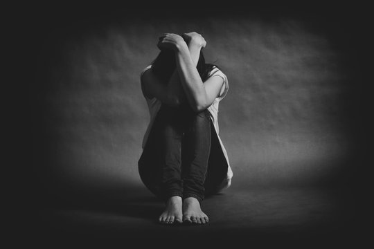 Teenager girl with depression sitting alone on the floor in the dark room. Black and white photo