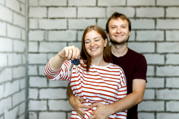 Young smiling couple showing keys to new home hugging looking at camera