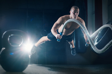 Man with battle ropes exercise in the fitness gym. Crossfit training workout. Sports functional training.
