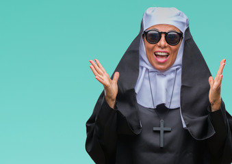Middle age senior catholic nun woman wearing sunglasses over isolated background celebrating crazy and amazed for success with arms raised and open eyes screaming excited. Winner concept