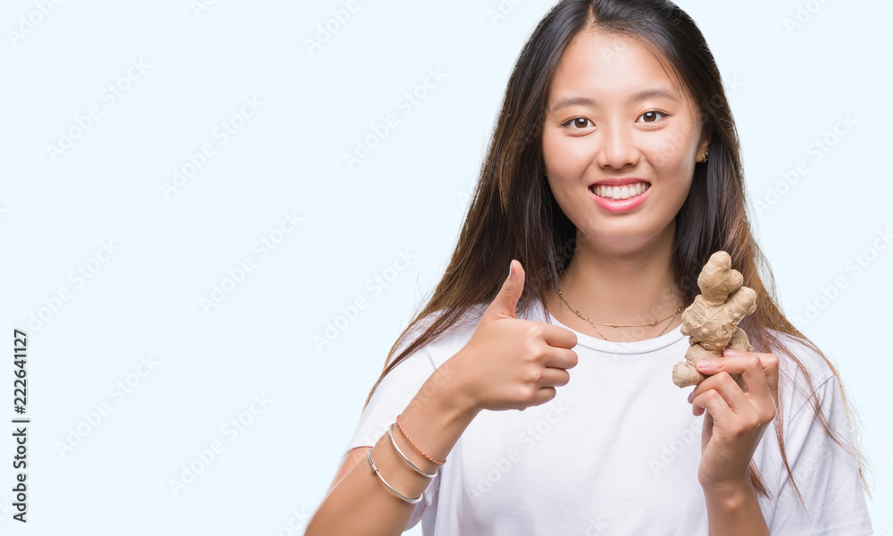 Sticker Young asian woman holding fresh organic over isolated background happy with big smile doing ok sign, thumb up with fingers, excellent sign