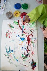 Top view of child creating a colourful abstract painting with a brush