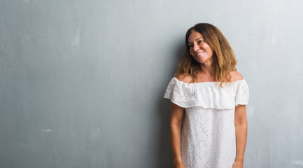 Fototapeta na wymiar Middle age hispanic woman standing over grey grunge wall looking away to side with smile on face, natural expression. Laughing confident.